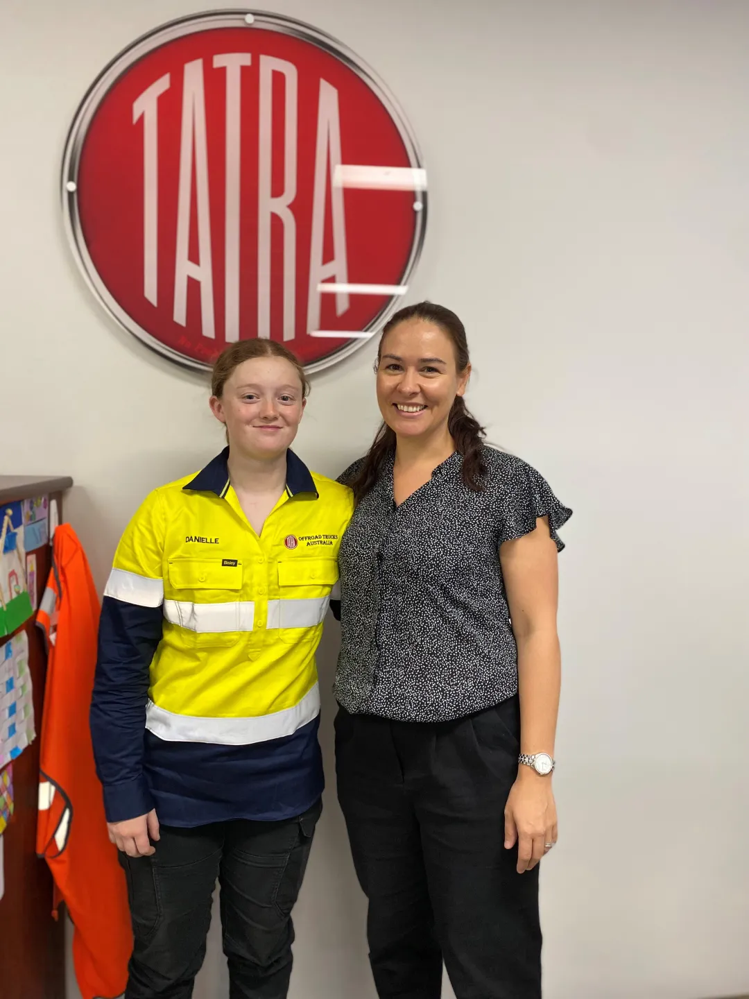 Employers How apprentices and trainees can grow your business Amber young smiling woman apprentice standing with employer looking at viewer in front of company sign indoors clothing human face indoor jeans person posing shoulder sign sleeve smile standing trousers wall woman