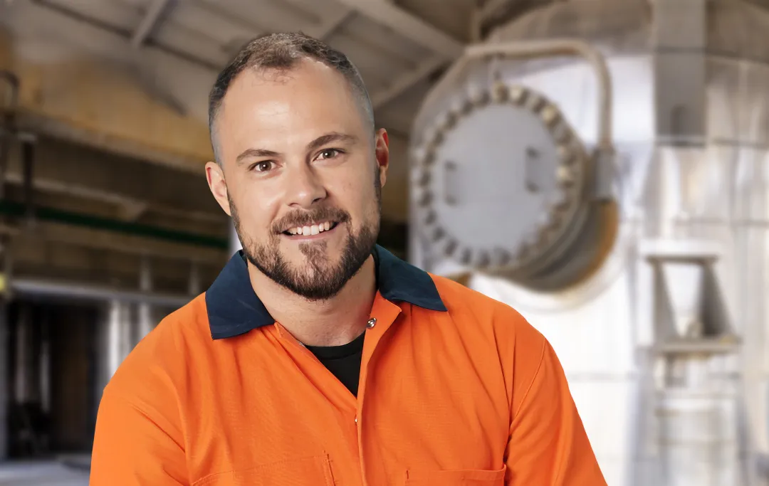 Boiler maker wearing orange work shirt standing by boiler