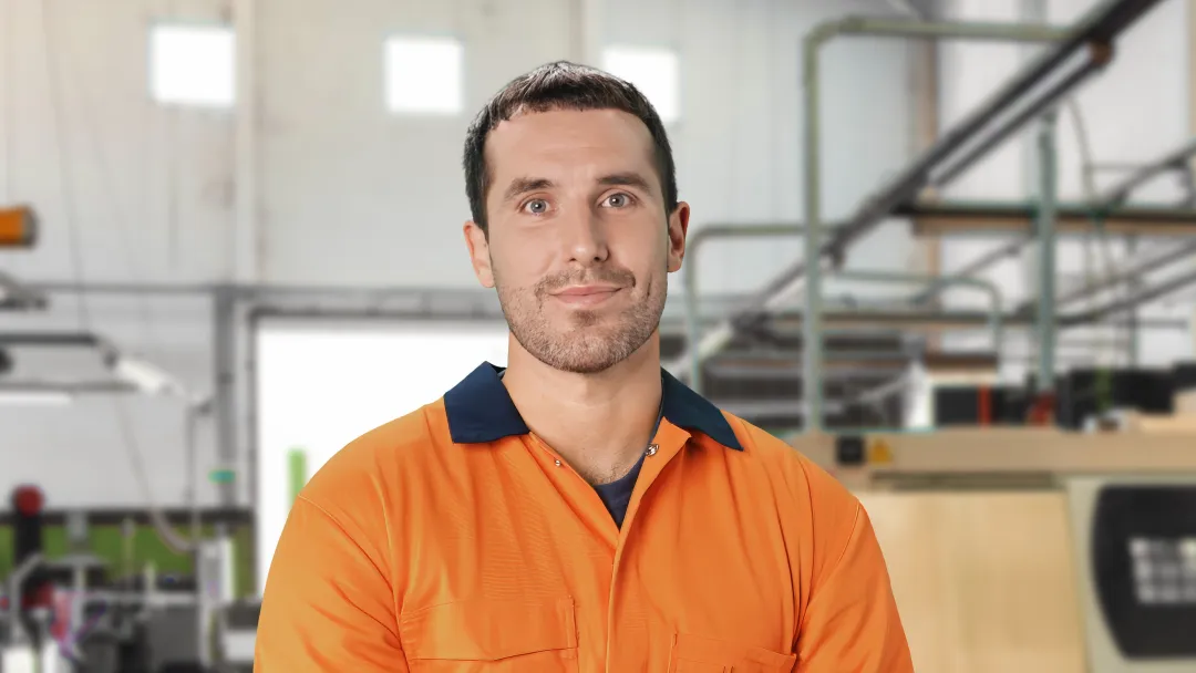 Mechanical fitter wearing orange work shirt standing in worksite surrounded by shelving