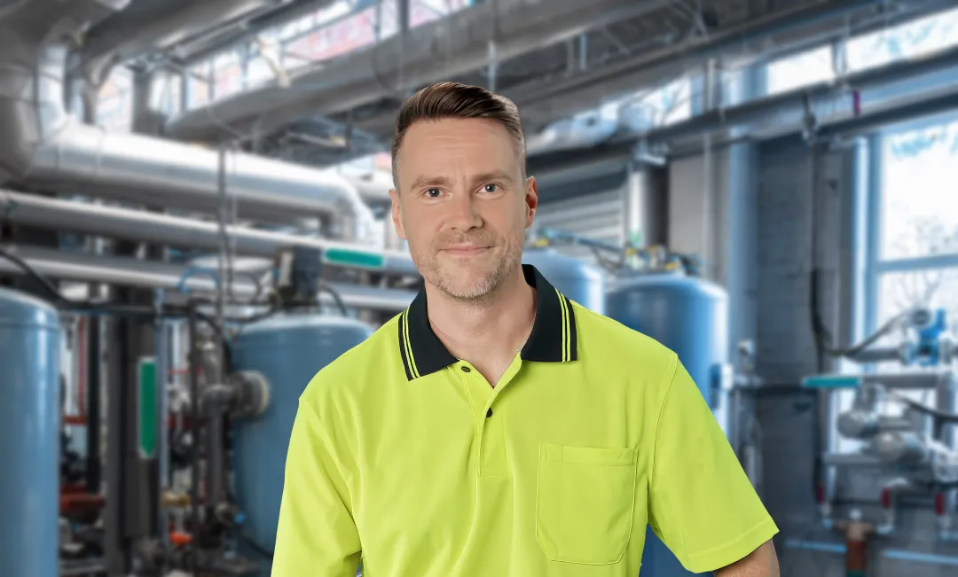 Plumber wearing work shirt surrounded by pipes and water systems
