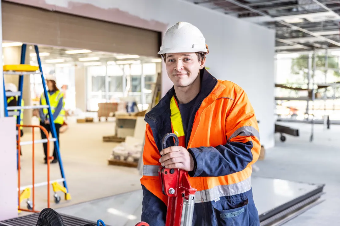 Young male in safety gear holding a tool on a construction site.