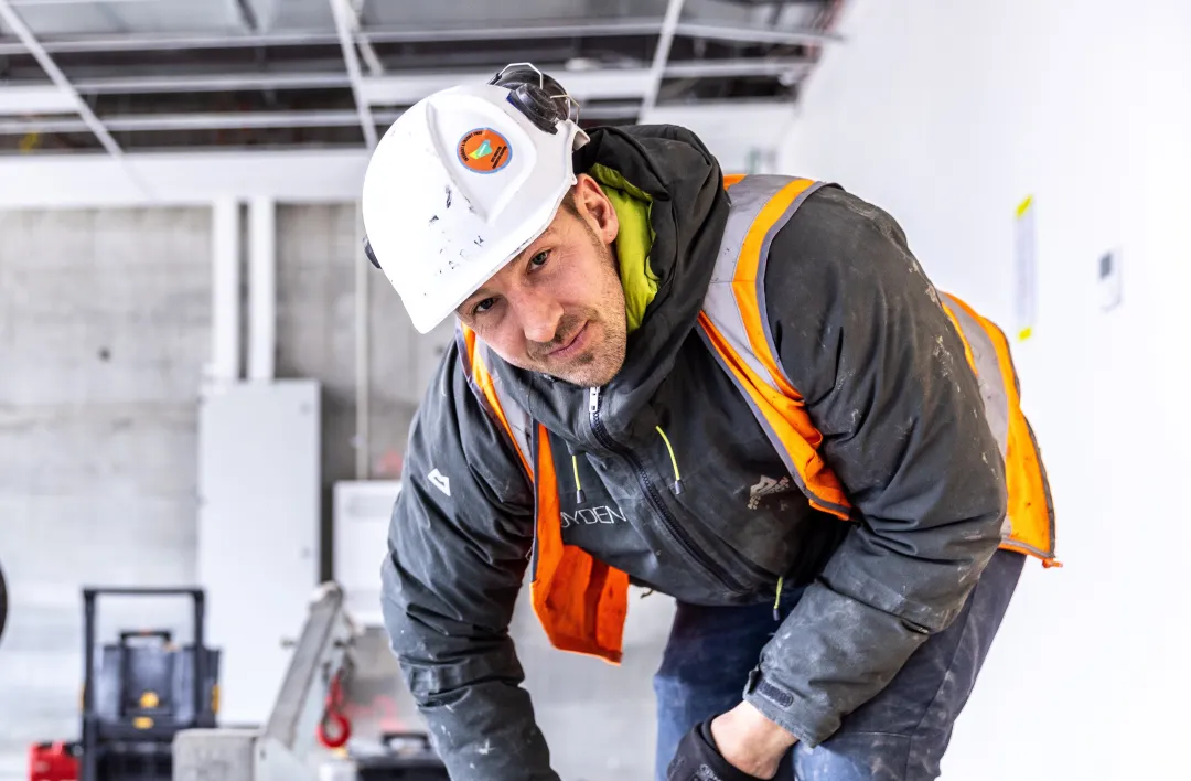 Worker in hard hat and safety vest bending down inside a construction site