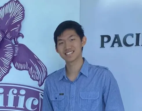 Eric wearing a blue button up dress shirt standing in front of a banner