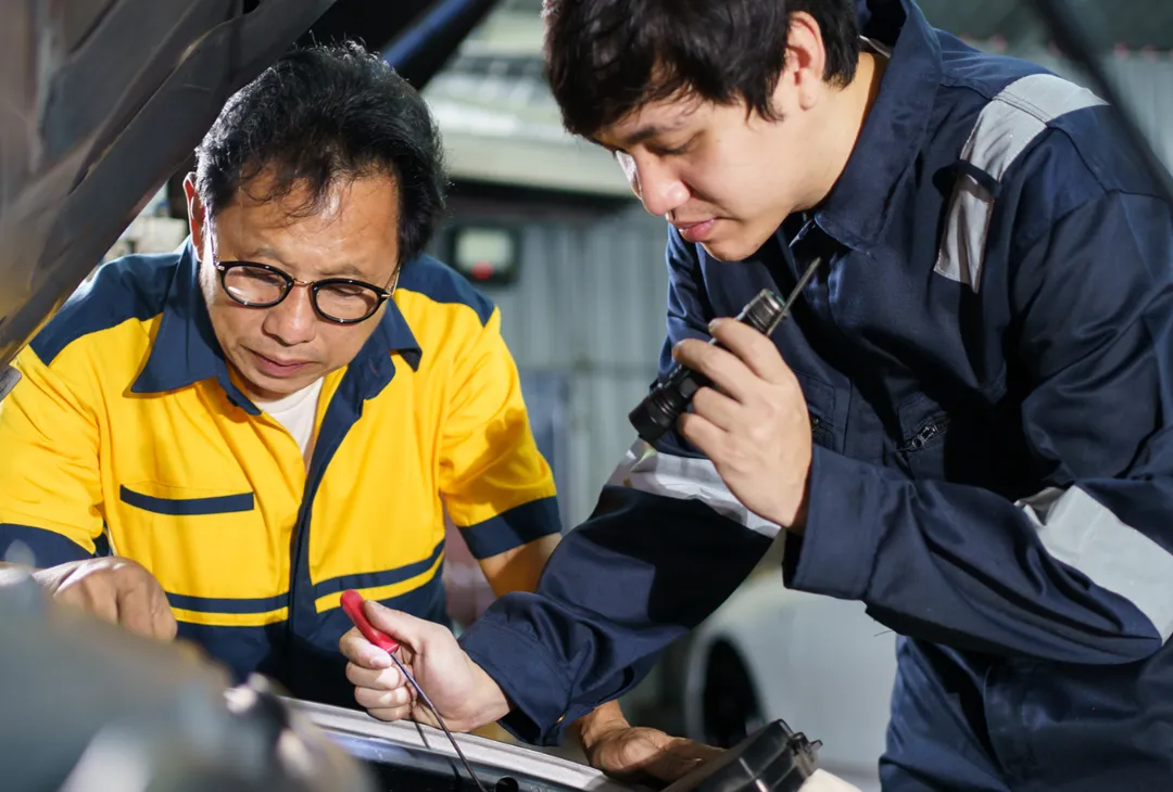 Two mechanics inspecting a car engine together.