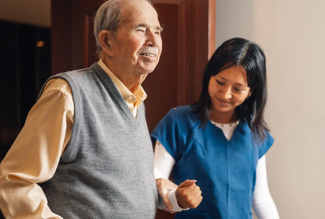A healthcare worker assisting an elderly man as they walk together.