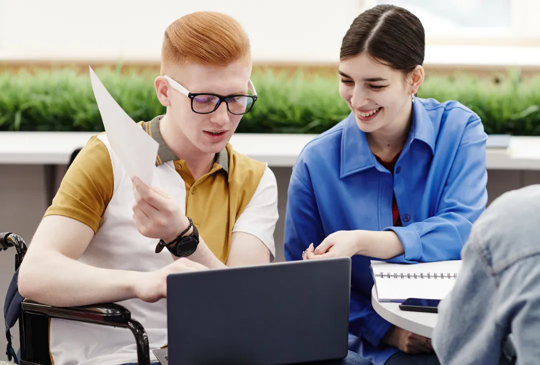 A disability support worker assisting a man in a wheelchair with his laptop.