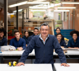 Man in foreground with hands on desk and peers behind him