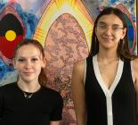 Two women standing in front of indigenous artwork wearing black
