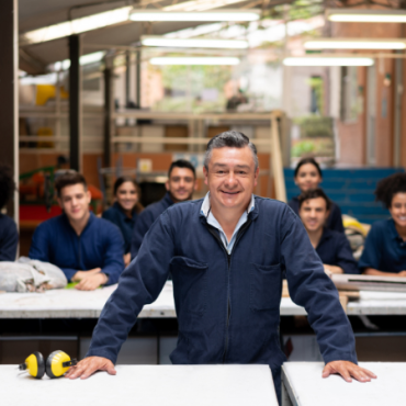 Man in foreground with hands on desk and peers behind him