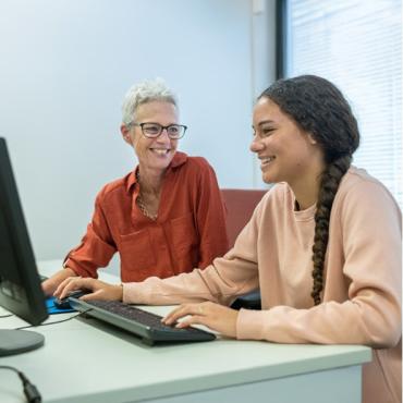Two people sitting at a desk typing on keyboards while they are smiling.