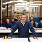 Man in foreground with hands on desk and peers behind him