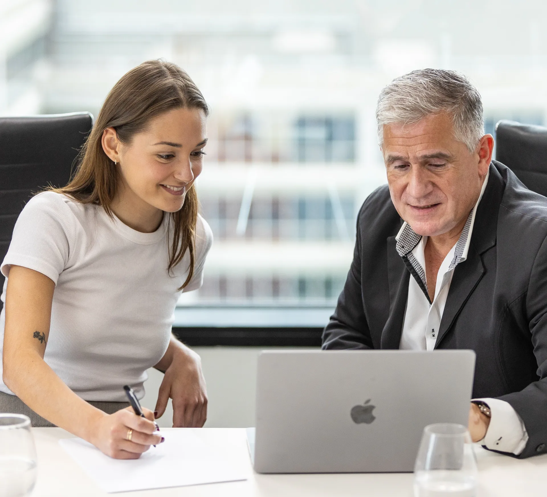 two people sitting at a desk looking at a laptop screen