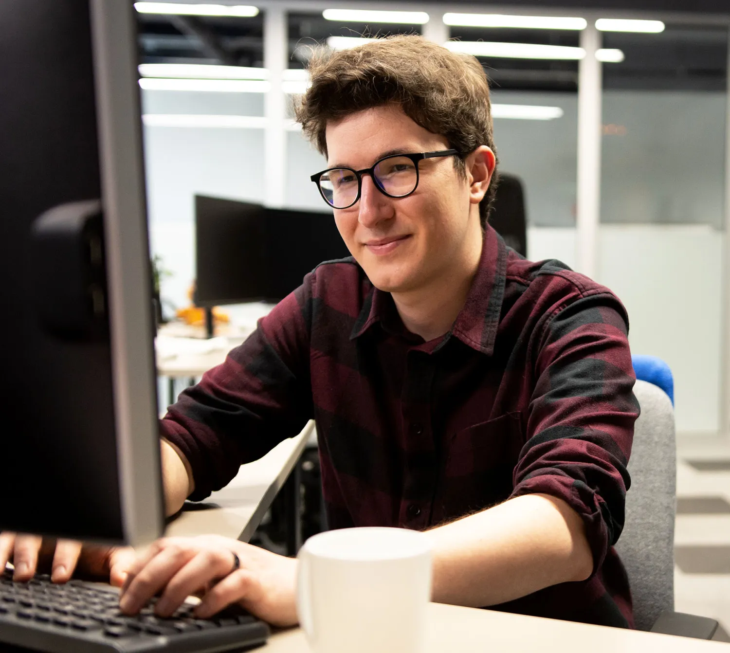Man wearing glasses and sweater sitting at a desk on a computer.