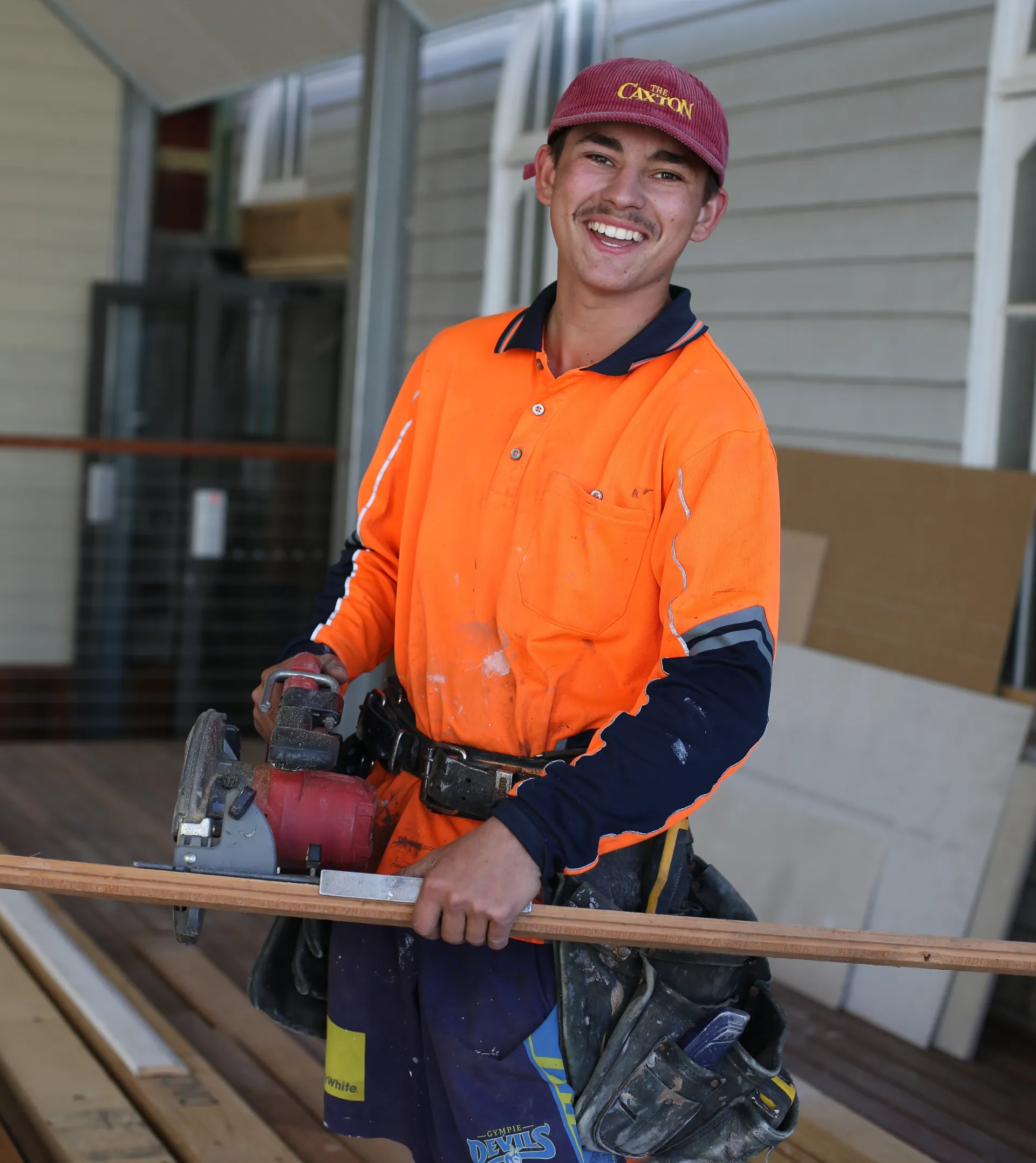 An apprentice wearing high visibility using a tool to cut wood.