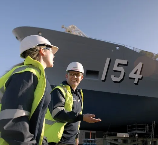 Two workers wearing high visibility vests and hard hats standing below a 154 ship