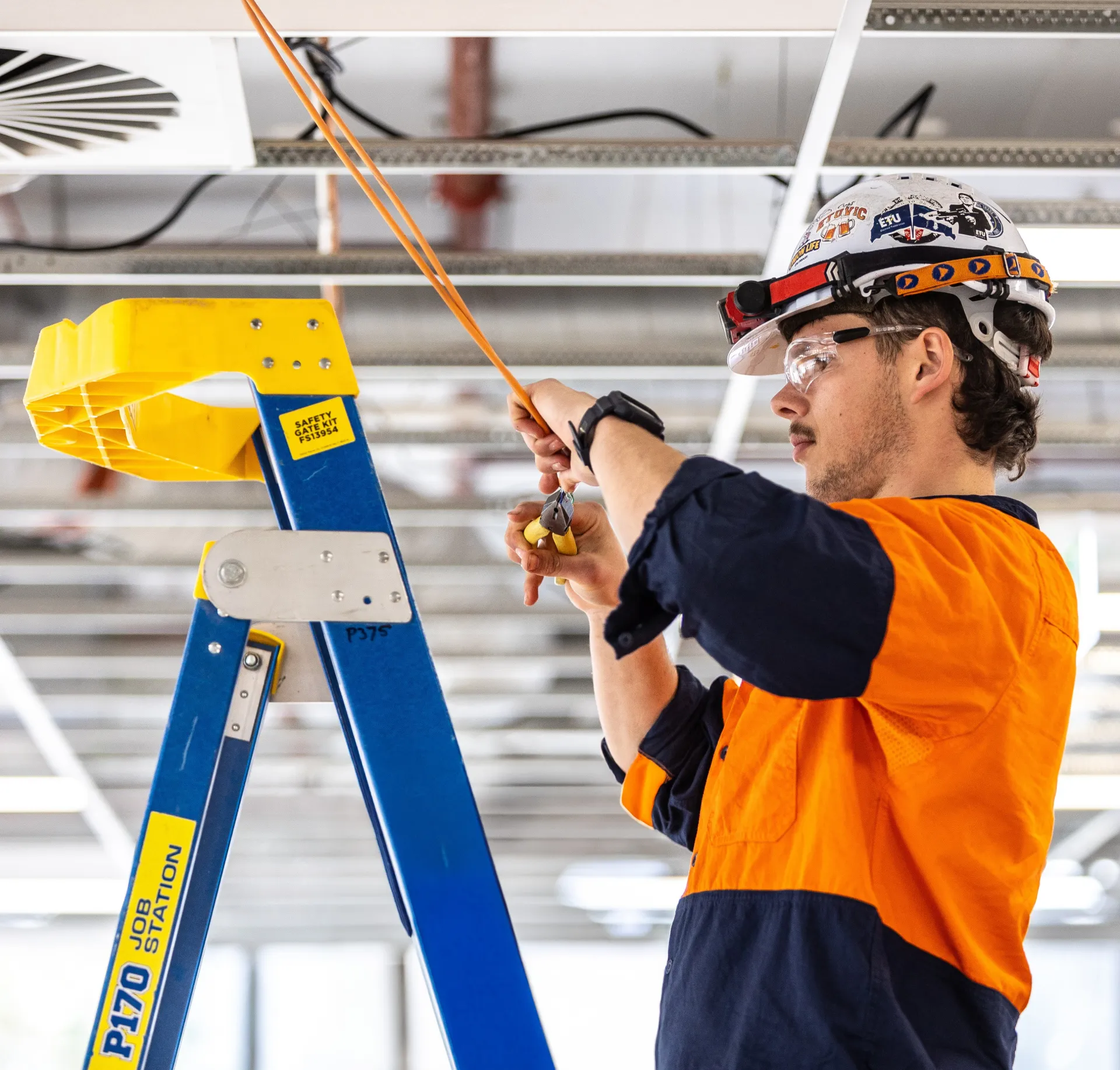 Electrician standing on a ladder working on electricals