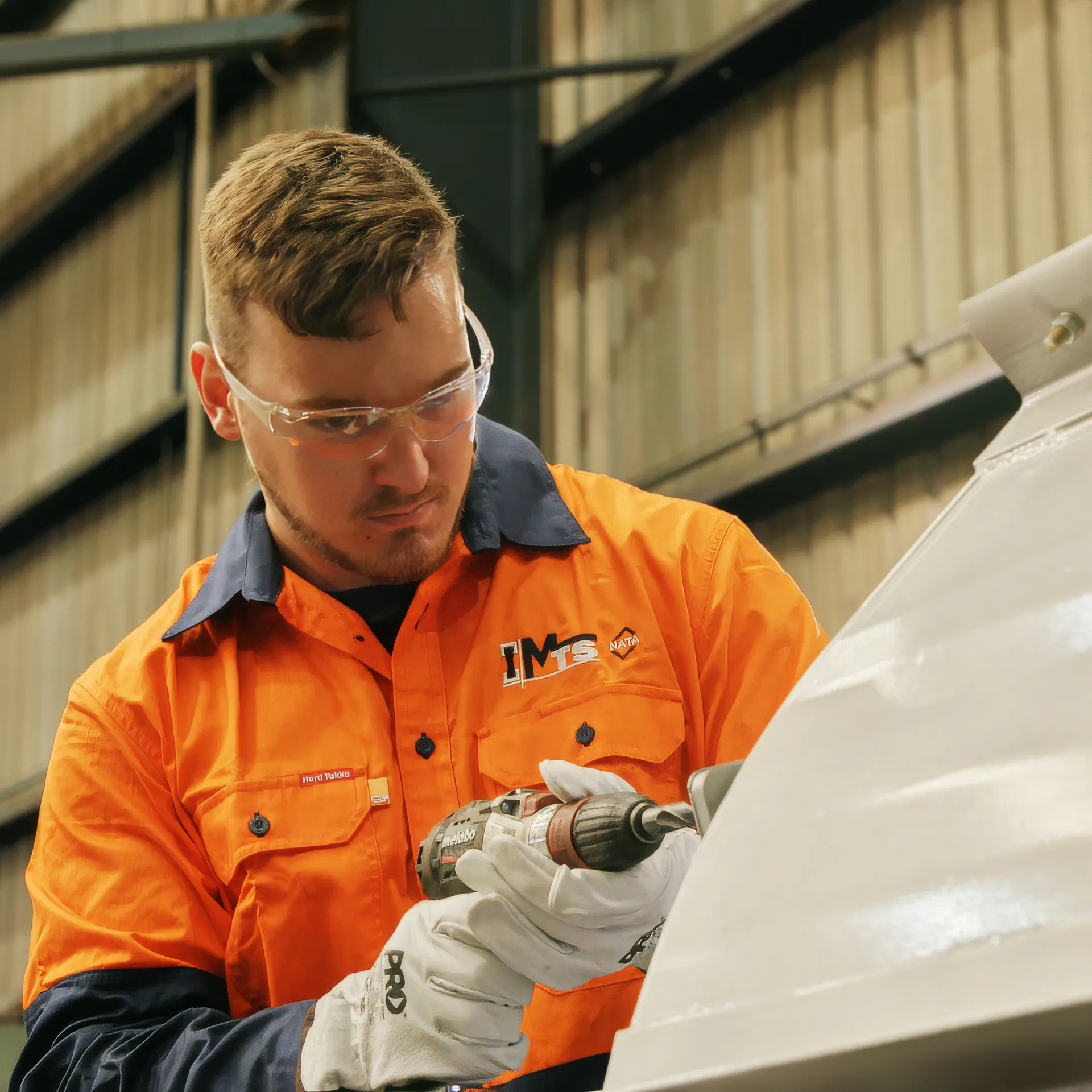 Warehouse worker wearing an orange high visibility jumper and protective glasses holding a power tool