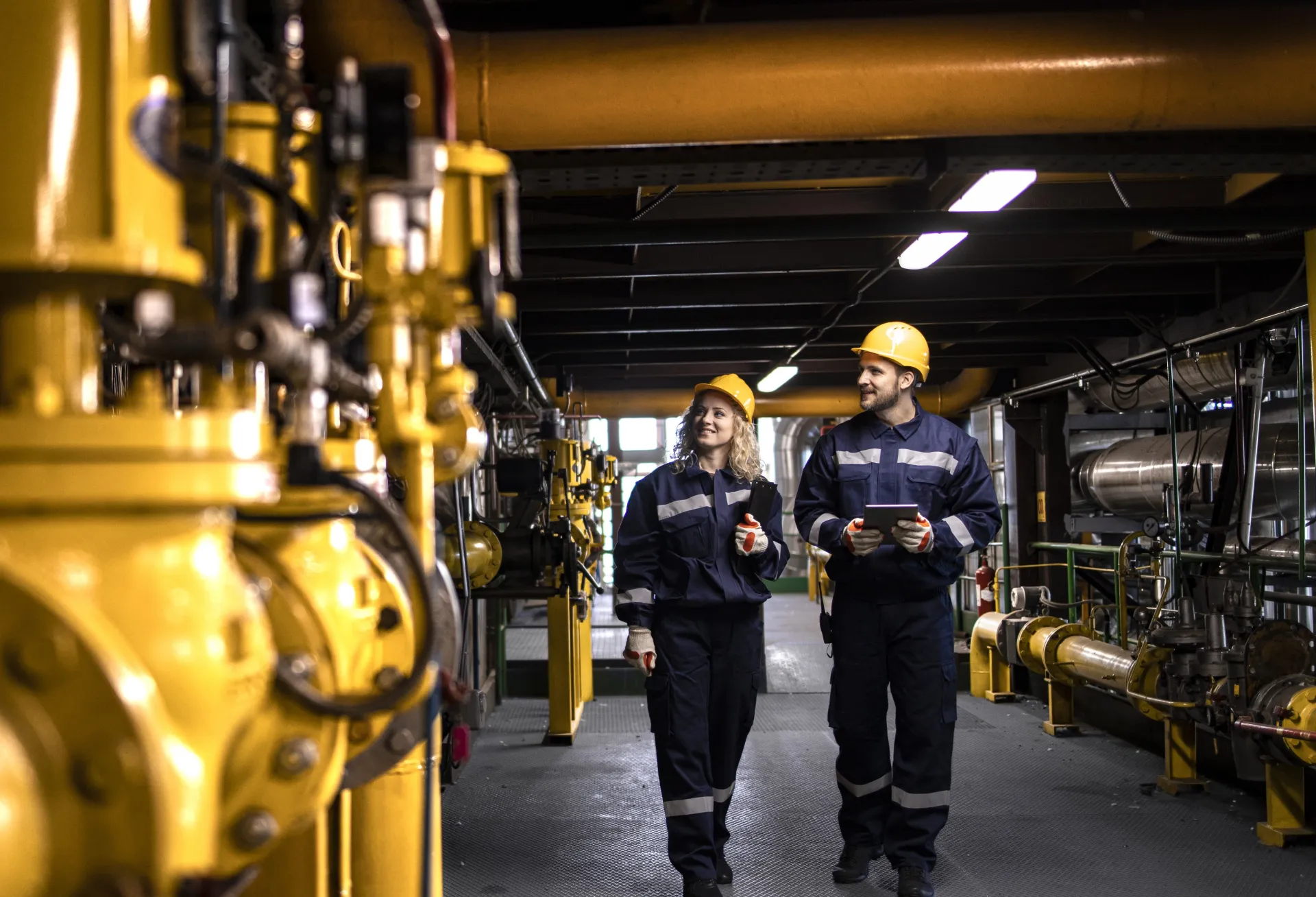 Two plumbers in hard hats walking through an industrial site.