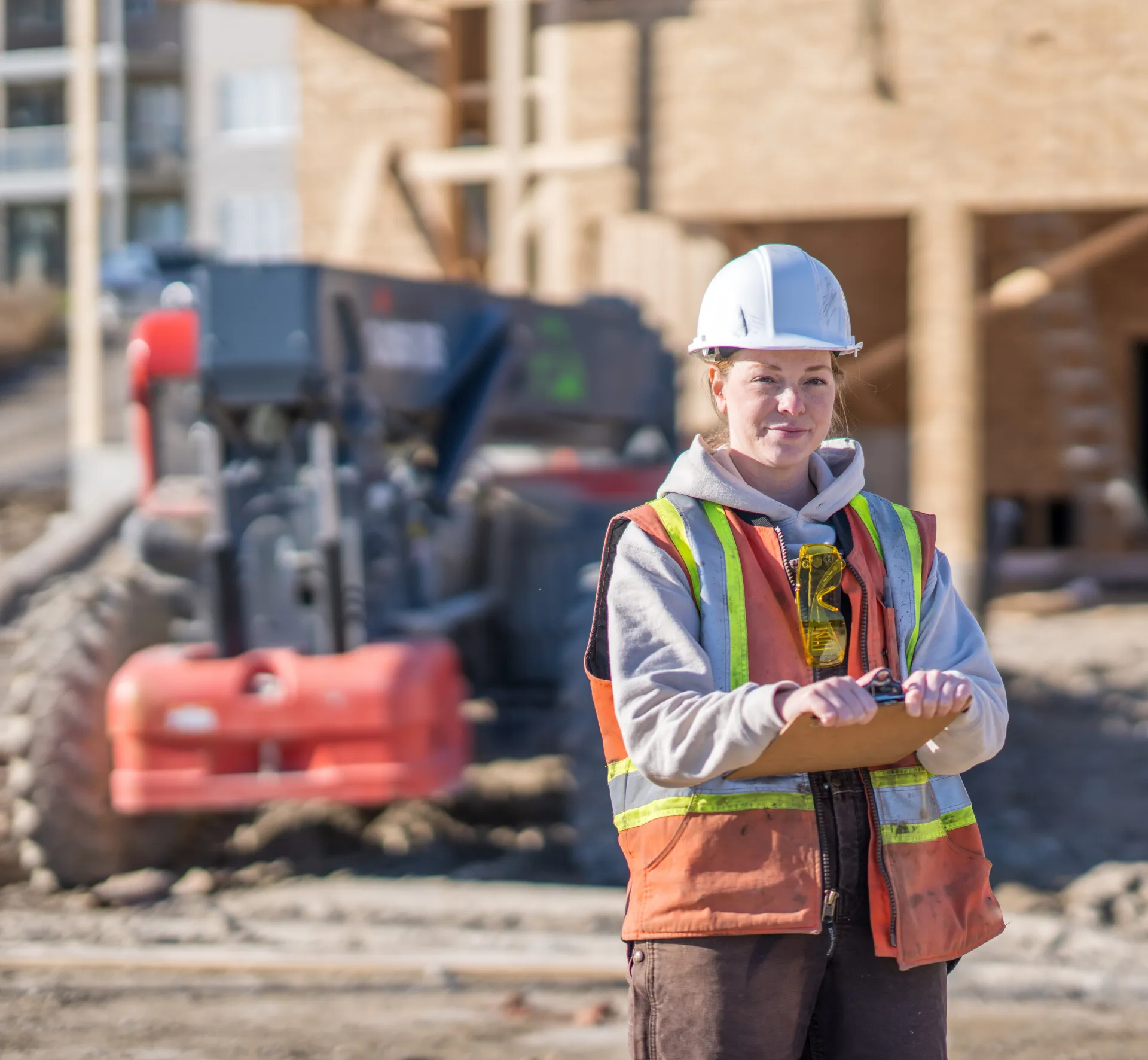 Construction worker at an outdoor worksite with machinery and buildings in the background