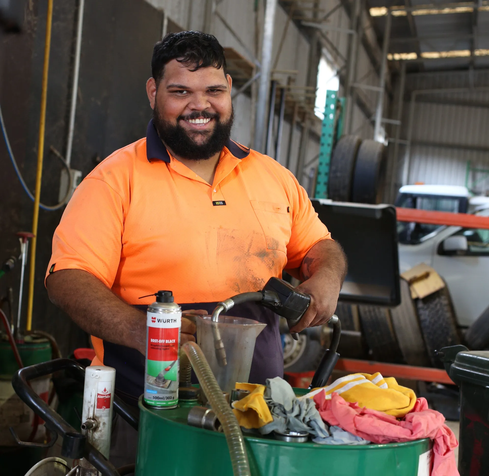Worker wearing orange high visibility workwear smiling while in a warehouse