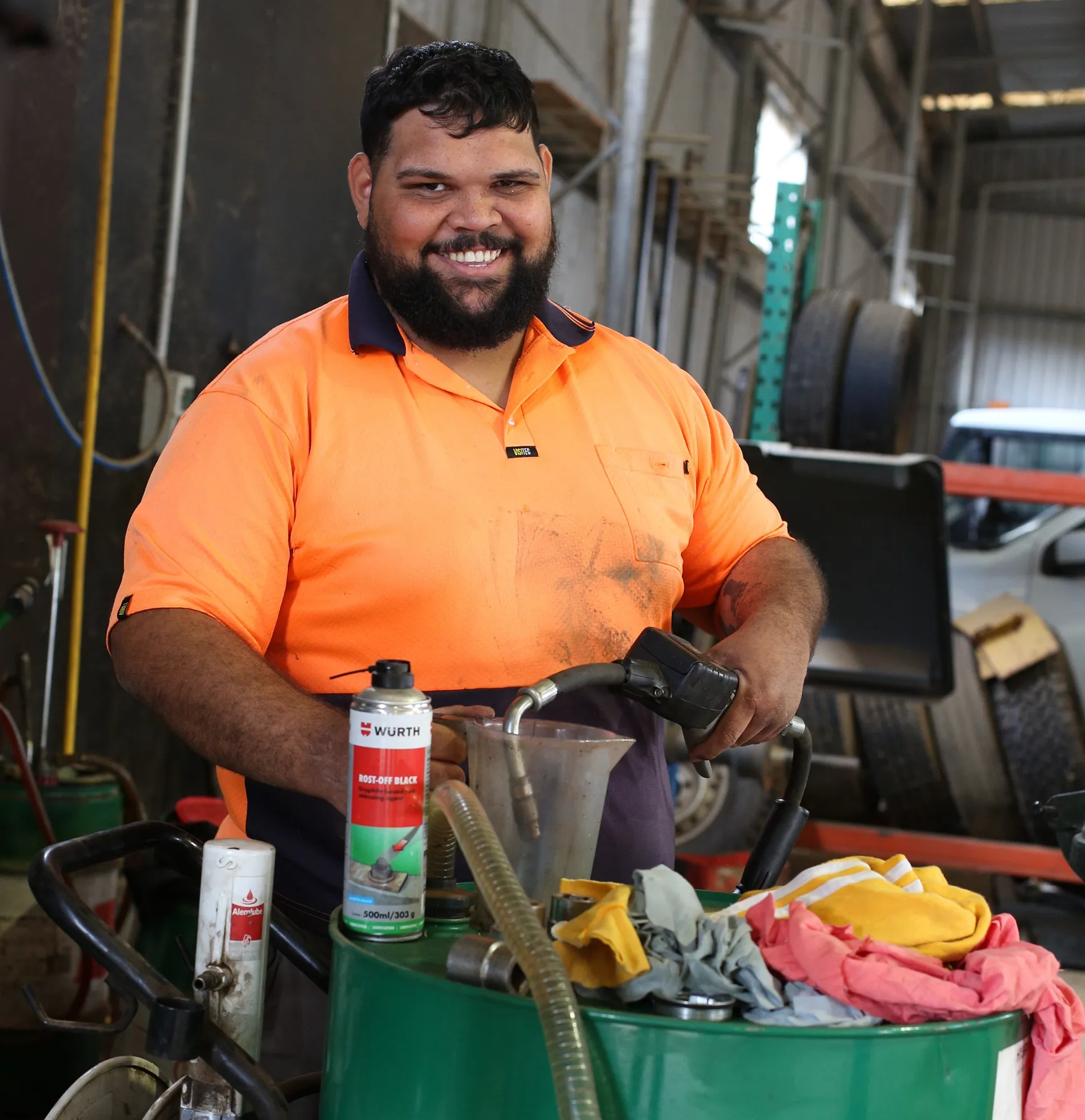 Worker wearing orange high visibility workwear smiling while in a warehouse