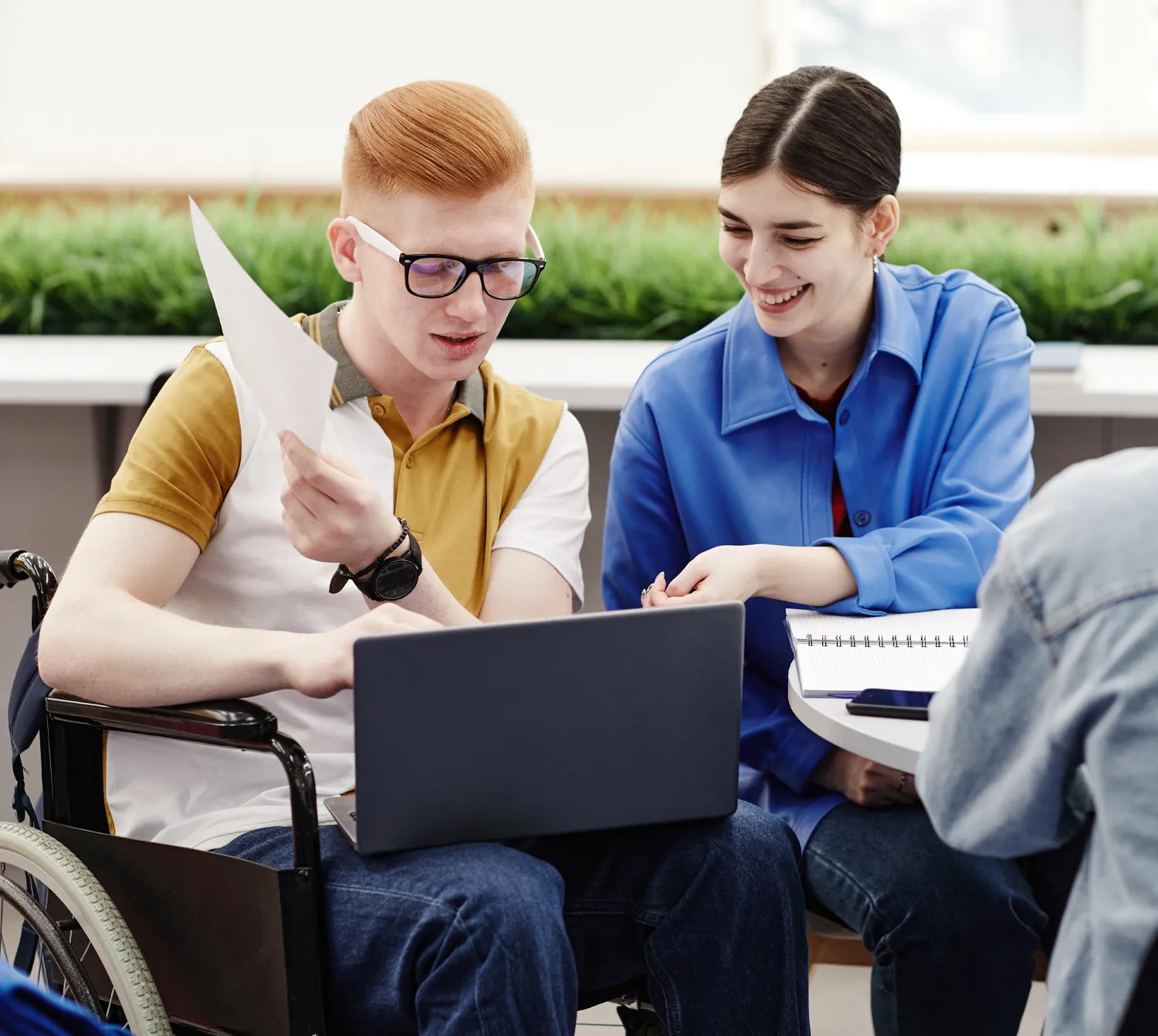 A disability support worker assisting a man in a wheelchair with his laptop.
