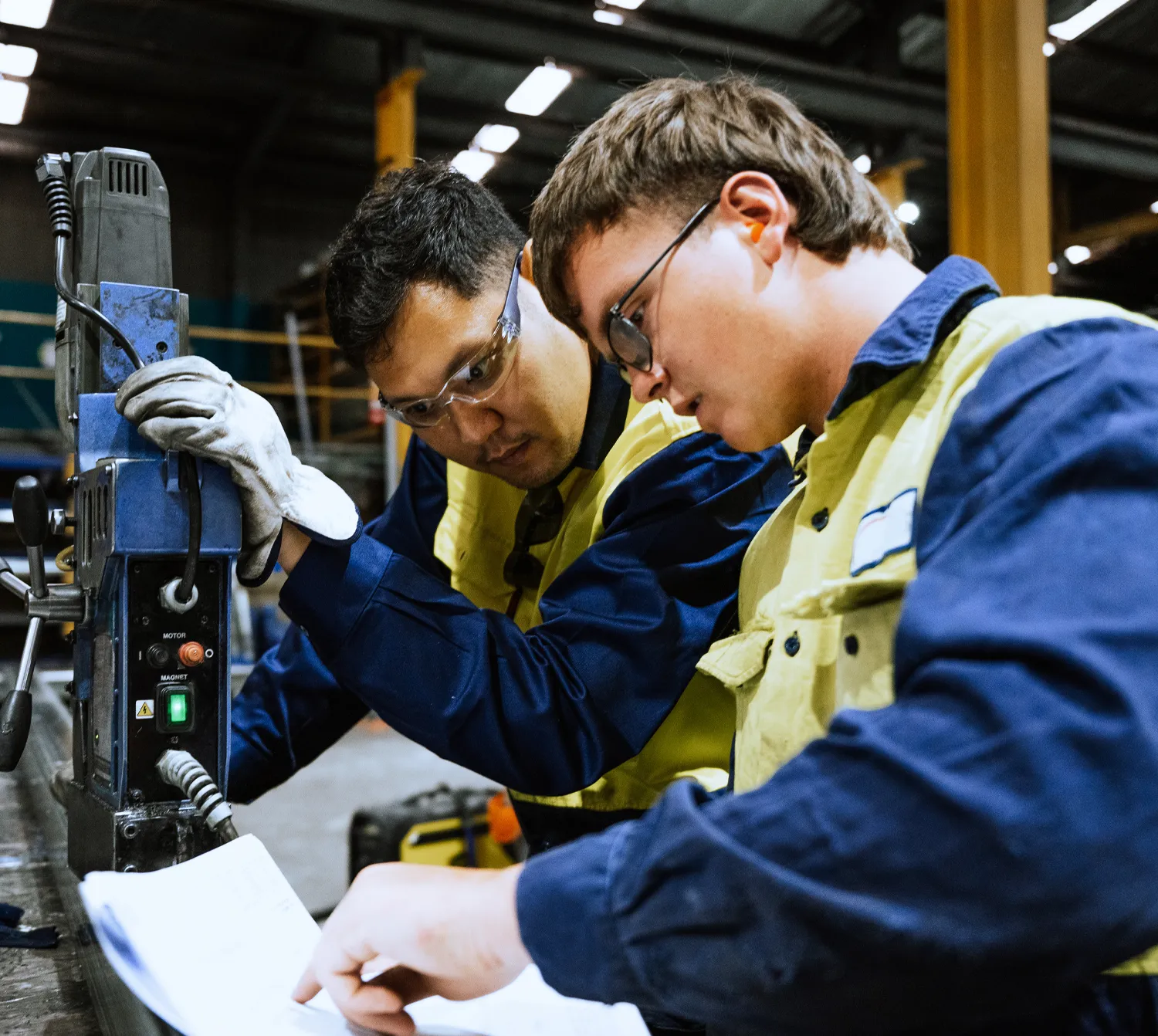 ChatGPT said:  An apprentice working with a supervisor in a workshop, reviewing plans and using machinery.