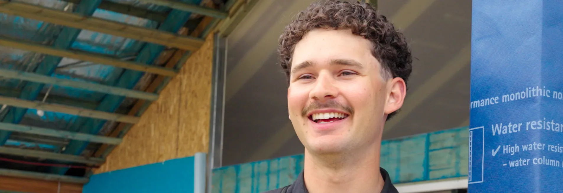 A male apprentice wearing a black collared shirt smiling