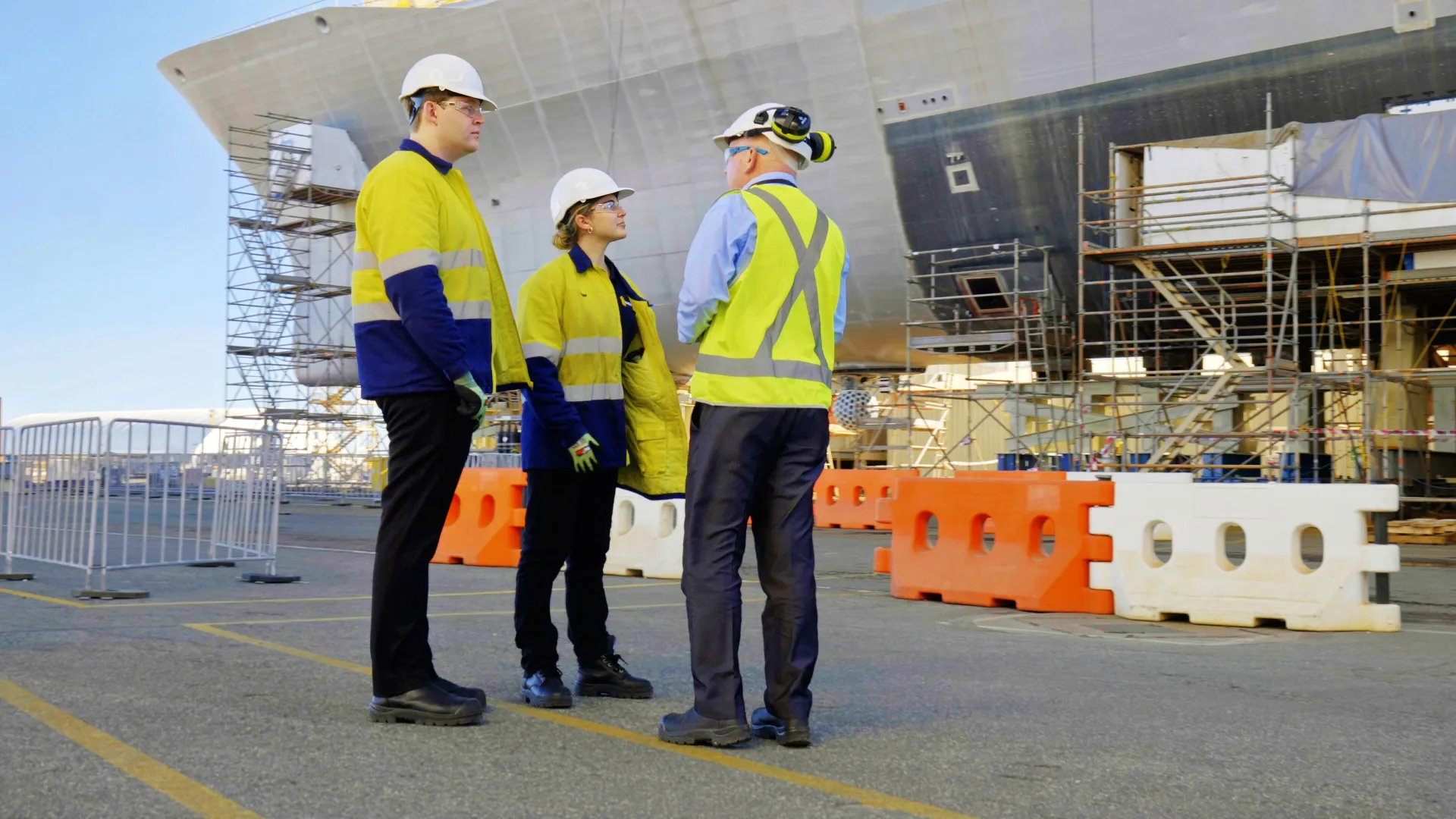 Workers wearing high visibility workwear and protective gear at a ship yard.