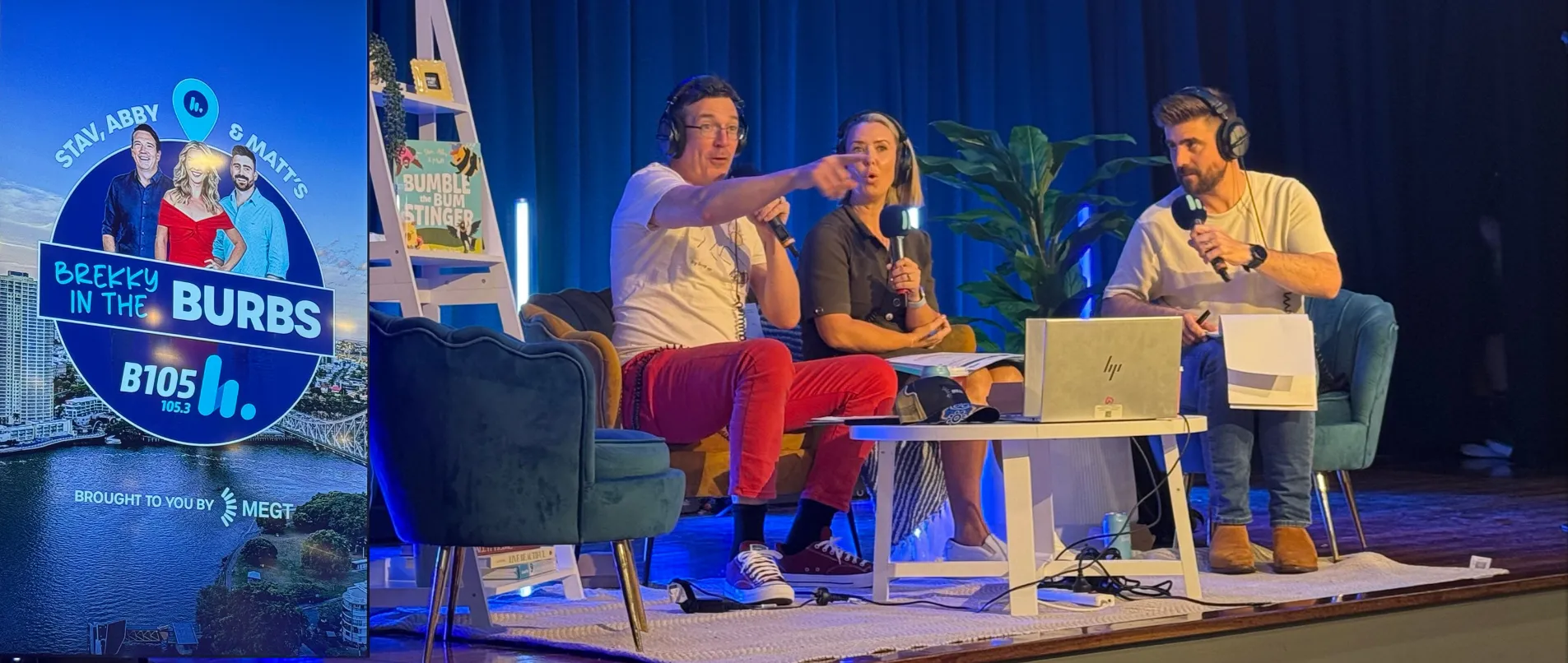 A live radio show setup on a stage features three people seated in armchairs, each wearing headsets and holding microphones.