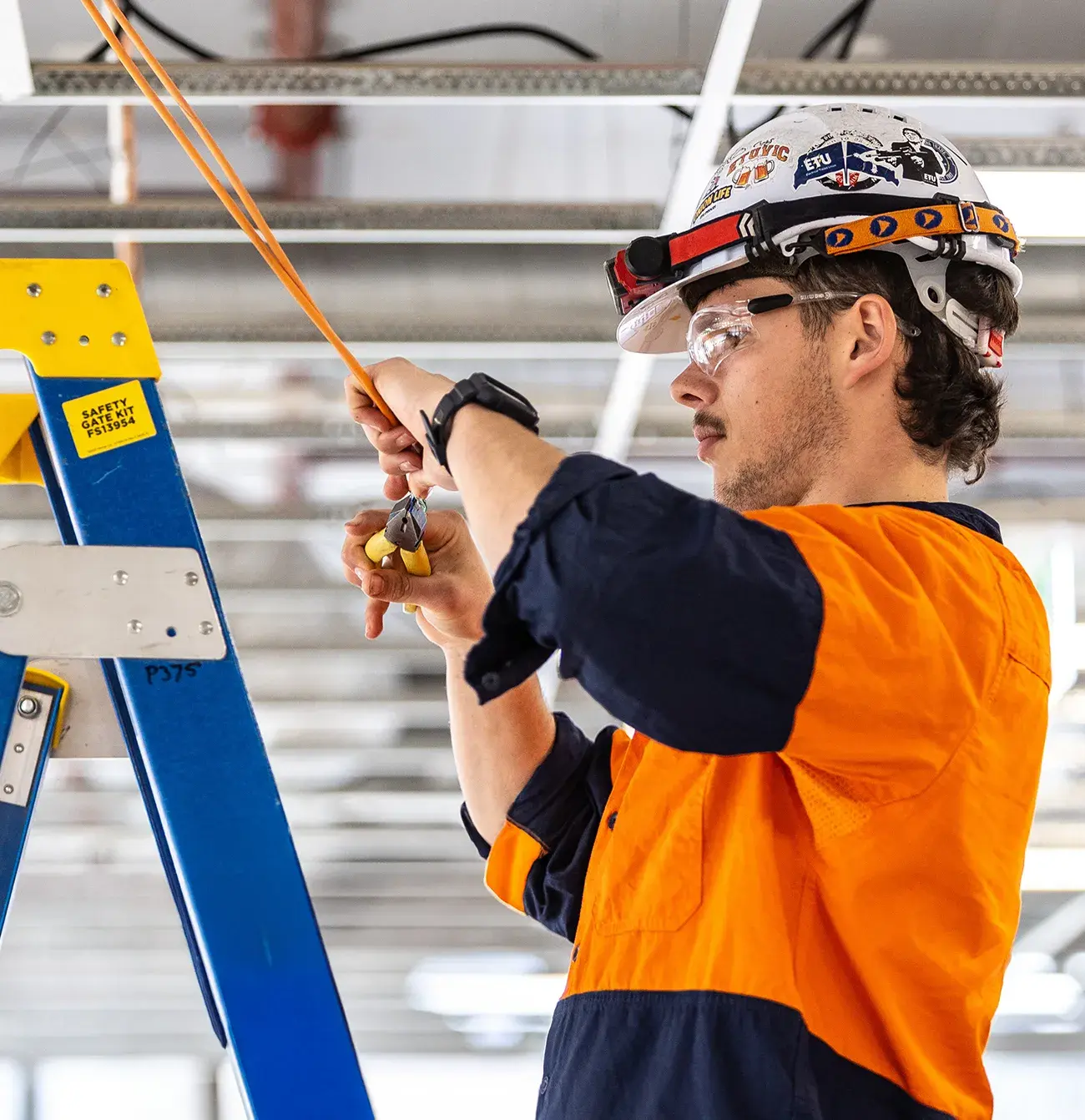 Electrician standing on a ladder working on electricals