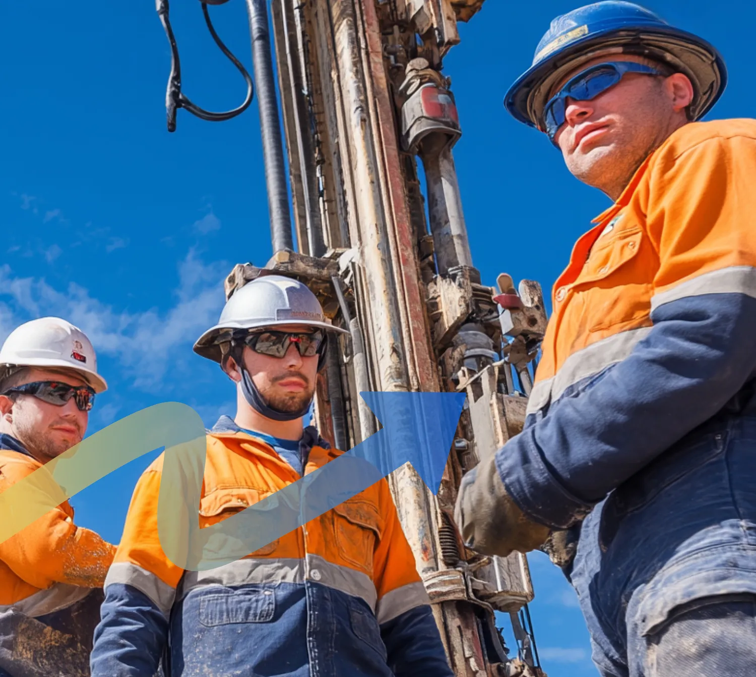 Workers in protective gear operating large drilling machinery under a clear blue sky.