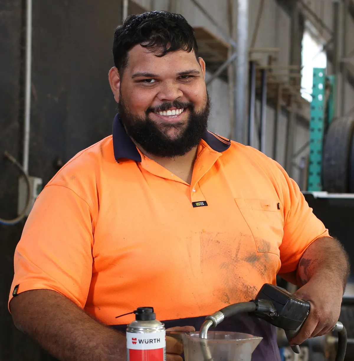 Person wearing a high‑visibility work shirt holding equipment in a workshop.