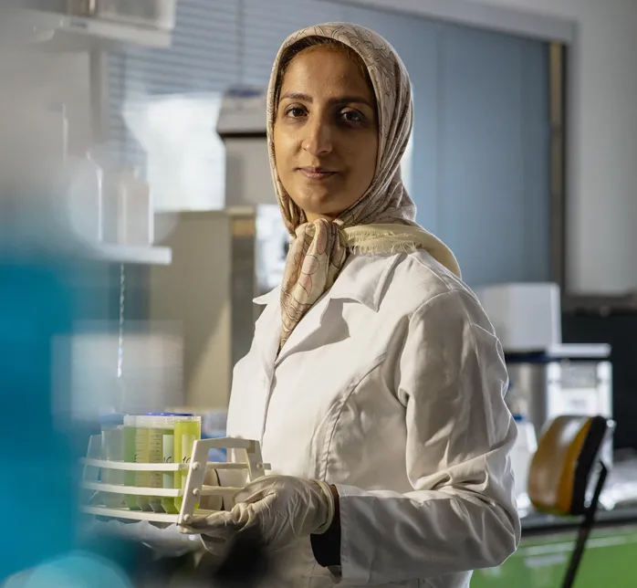 Person in a lab coat holding a rack of test tubes in a laboratory.