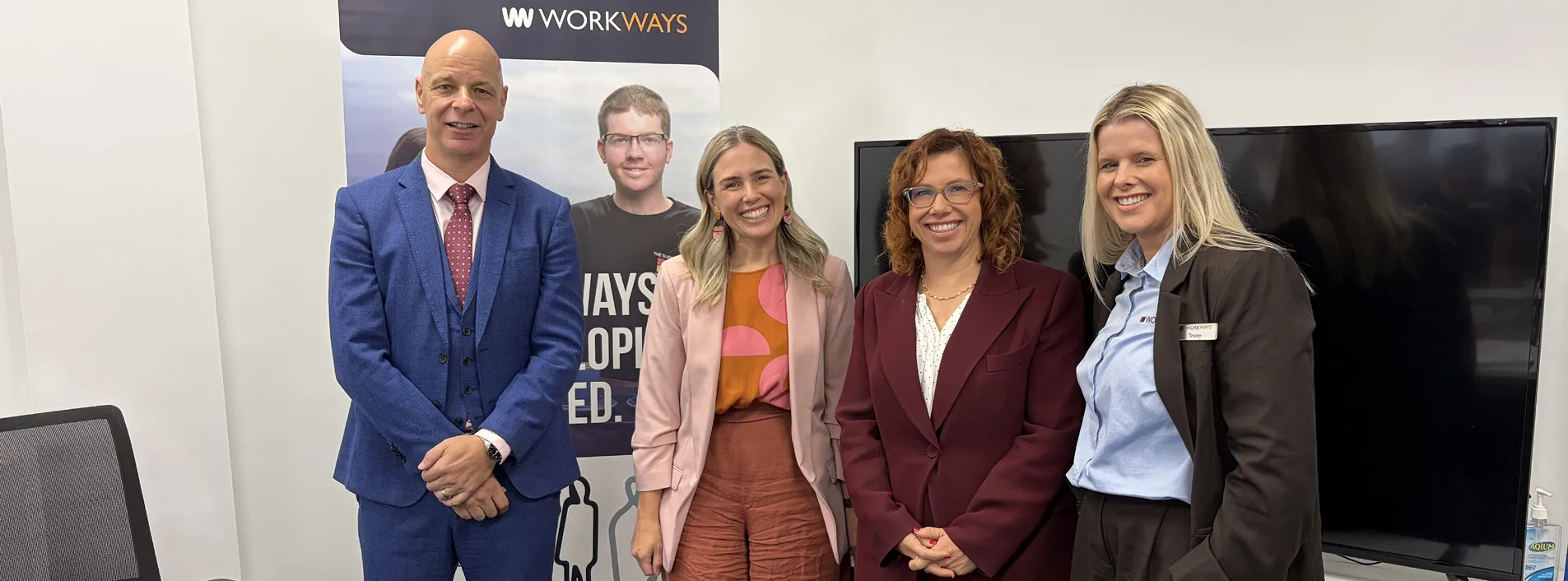 Four professionals standing indoors in front of Workways banner and display screen.