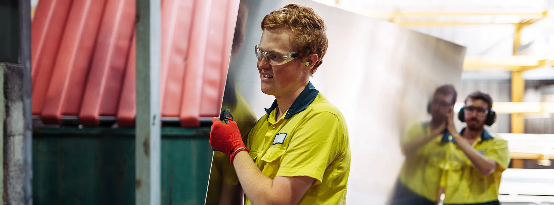Two employees holding a large metal sheet.