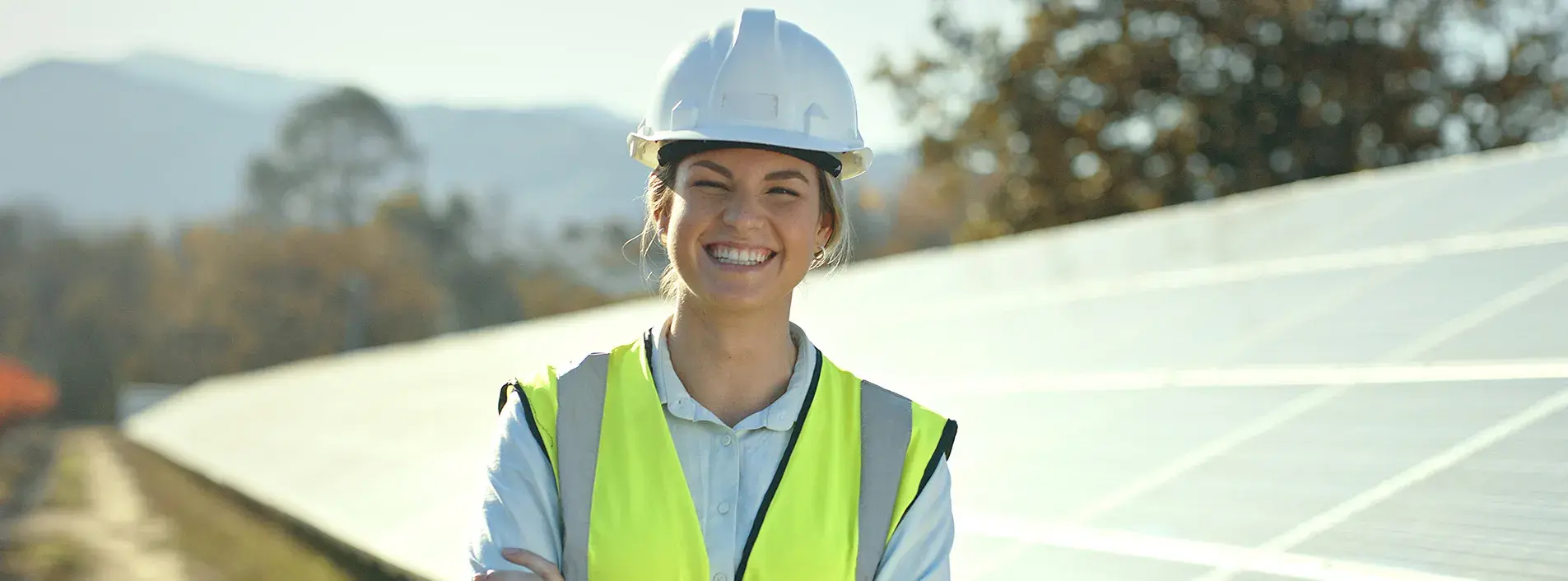 Female blue collar worker smiling in front of large solar panels