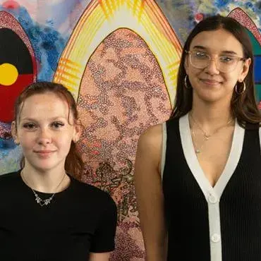Two young people standing in front of Aboriginal-style artwork